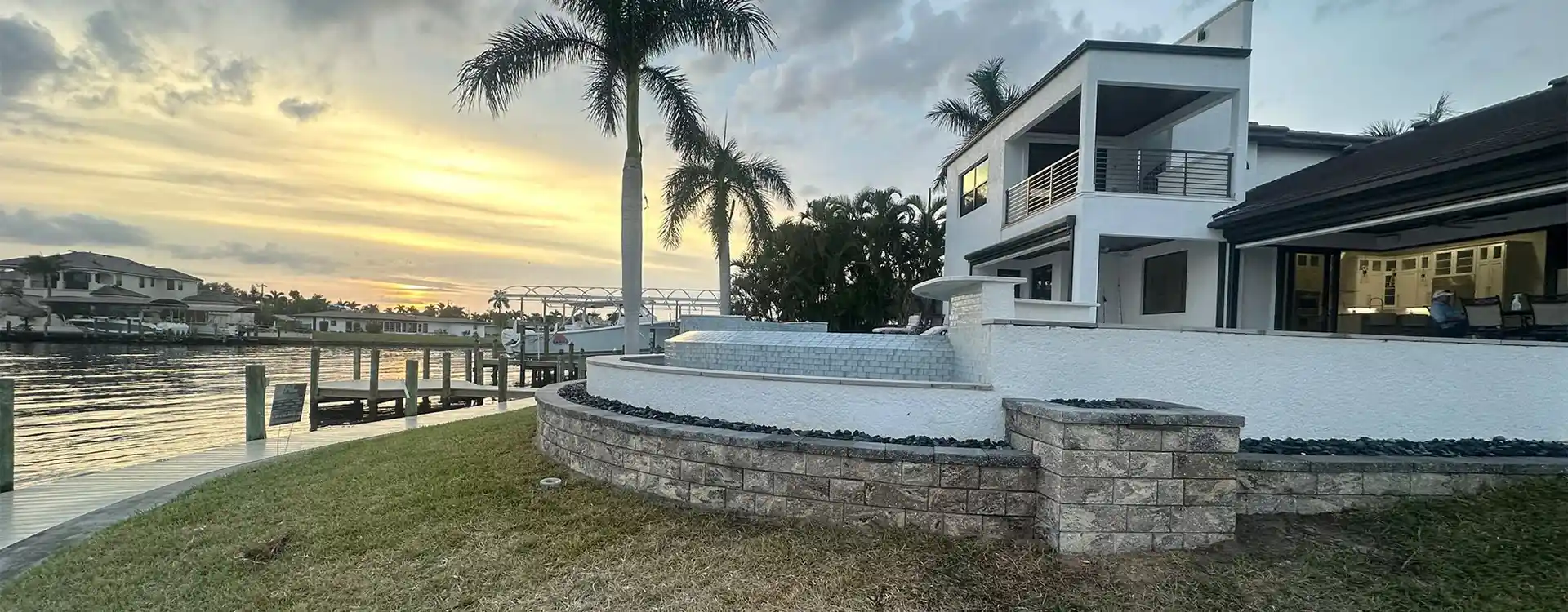 Curved stone retaining wall around a waterfront pool deck at sunset